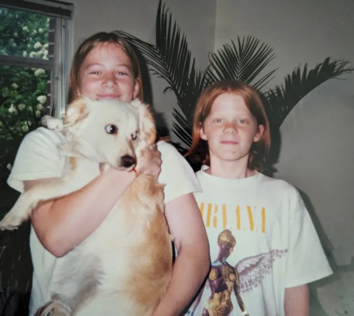 Shane and David as kids at home, one holding a white and tan dog