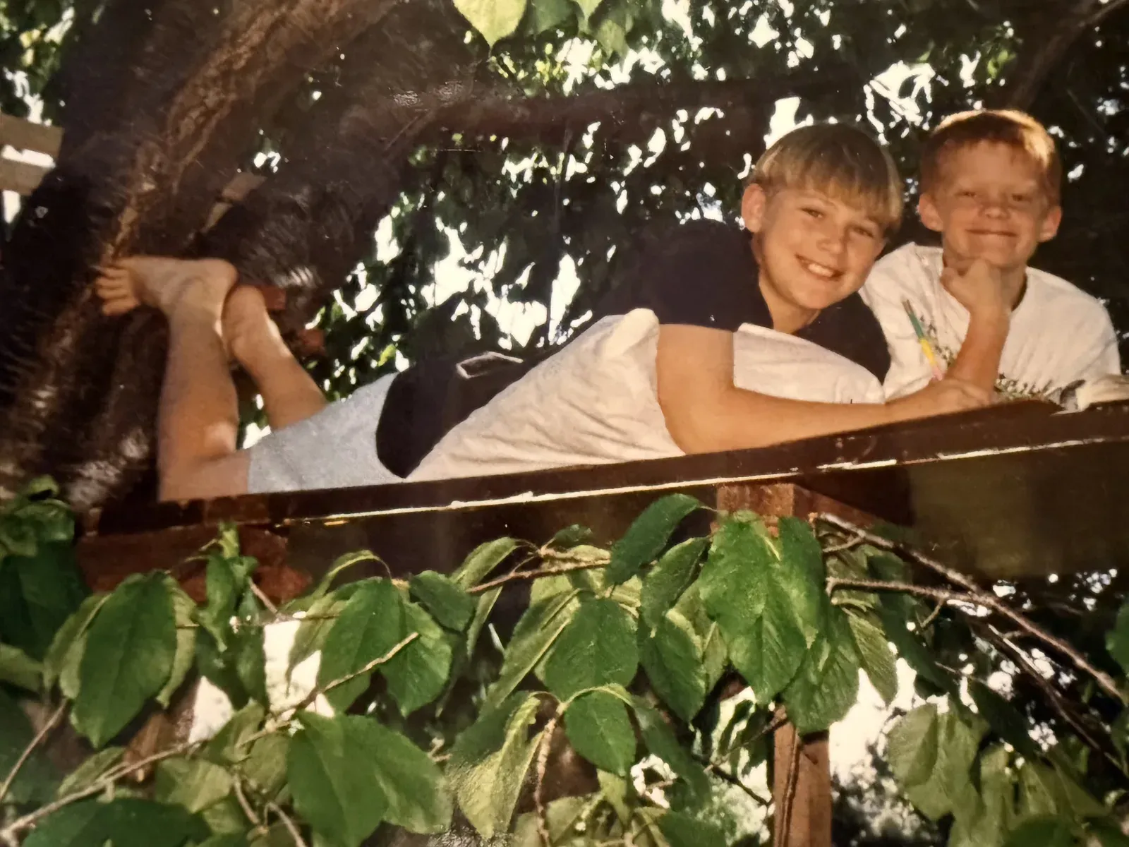 Shane and David as kids, lying on a treehouse platform high in a leafy tree